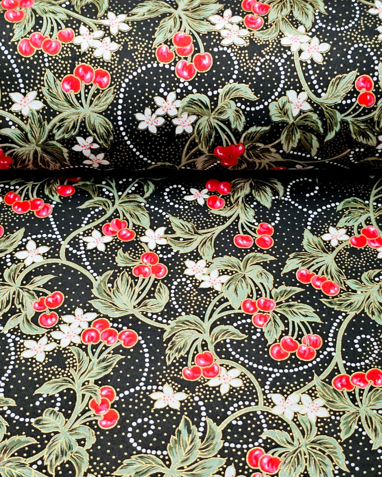 Japanese chiyogami paper featuring red cherries with white flowers and green leaves on a black background with metallic gold details.