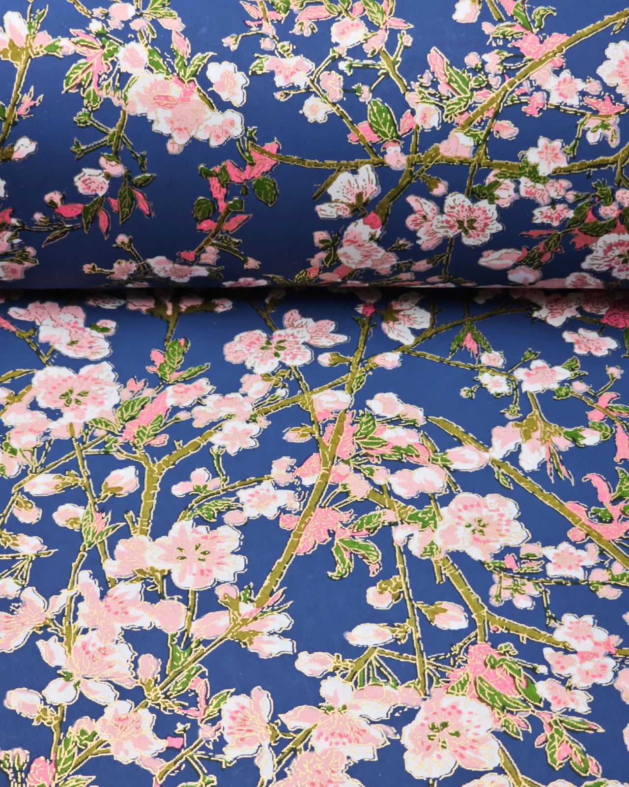 Japanese chiyogami paper featuring pink and white detailed plum blossoms with brown branches and green leaves on a dark blue background with metallic gold details.