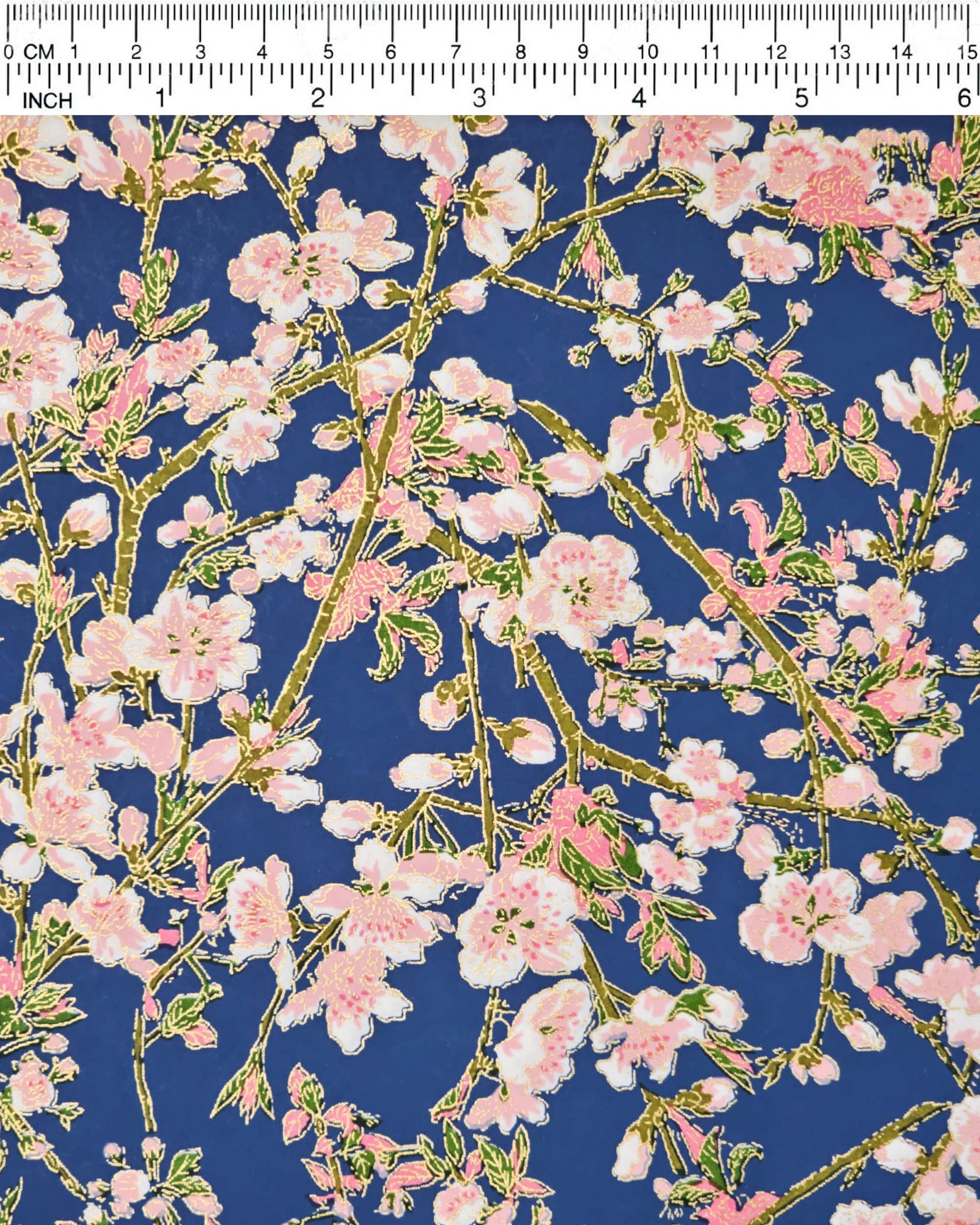 Japanese chiyogami paper featuring pink and white detailed plum blossoms with brown branches and green leaves on a dark blue background with metallic gold details.