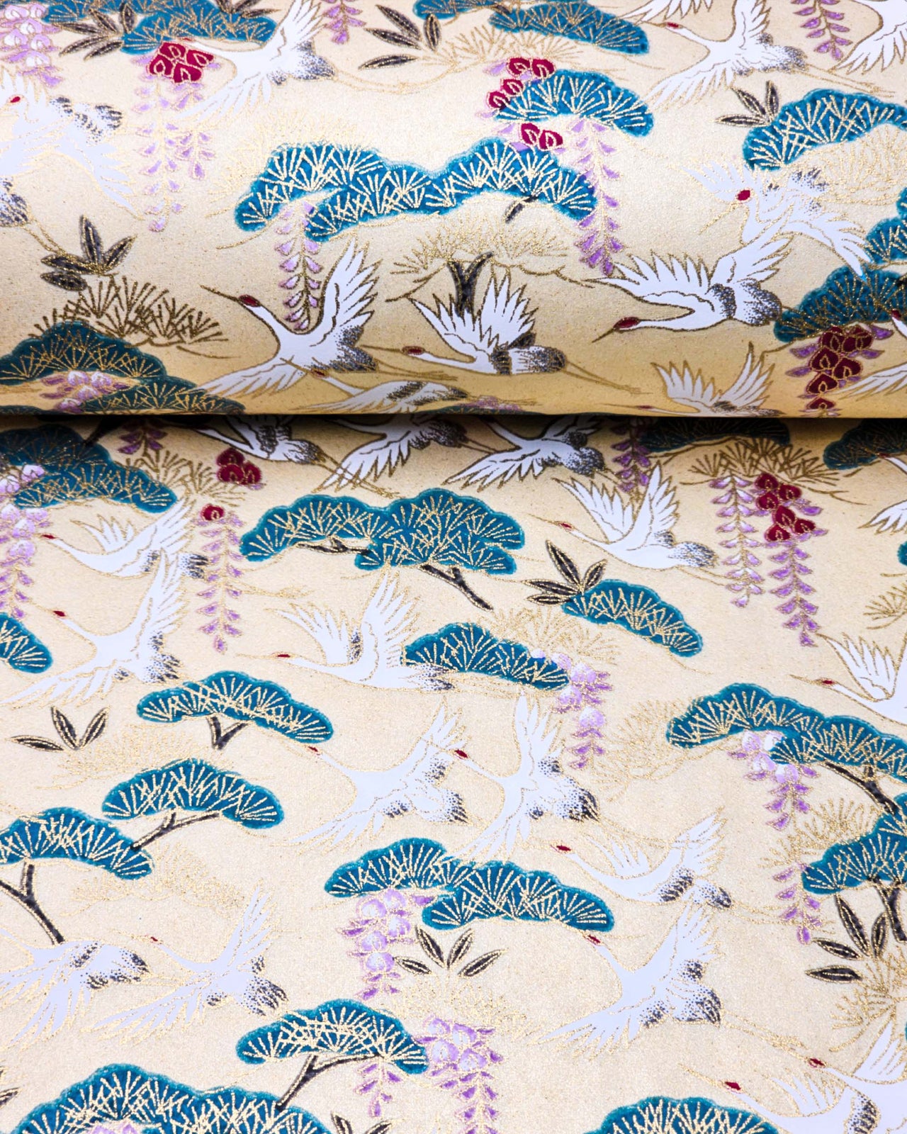 Japanese chiyogami paper featuring white flying cranes, purple and red wisteria, and green pine on a light shimmering gold background with metallic gold details.