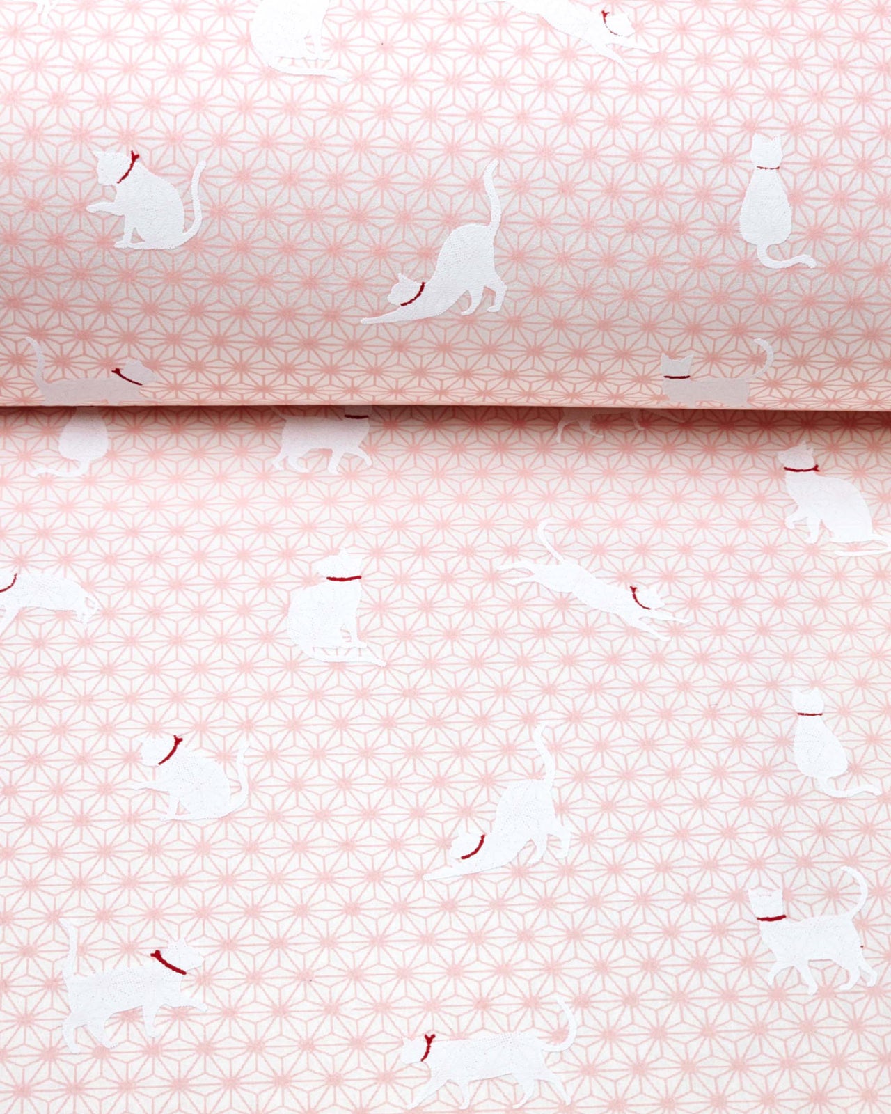 Japanese chiyogami paper featuring assorted white cats with red collars on a light pink asanoha (hemp leaf) background.
