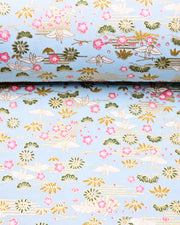 Japanese chiyogami paper featuring white origami cranes with green plants and pink plum blossoms on a light blue background with metallic gold details.