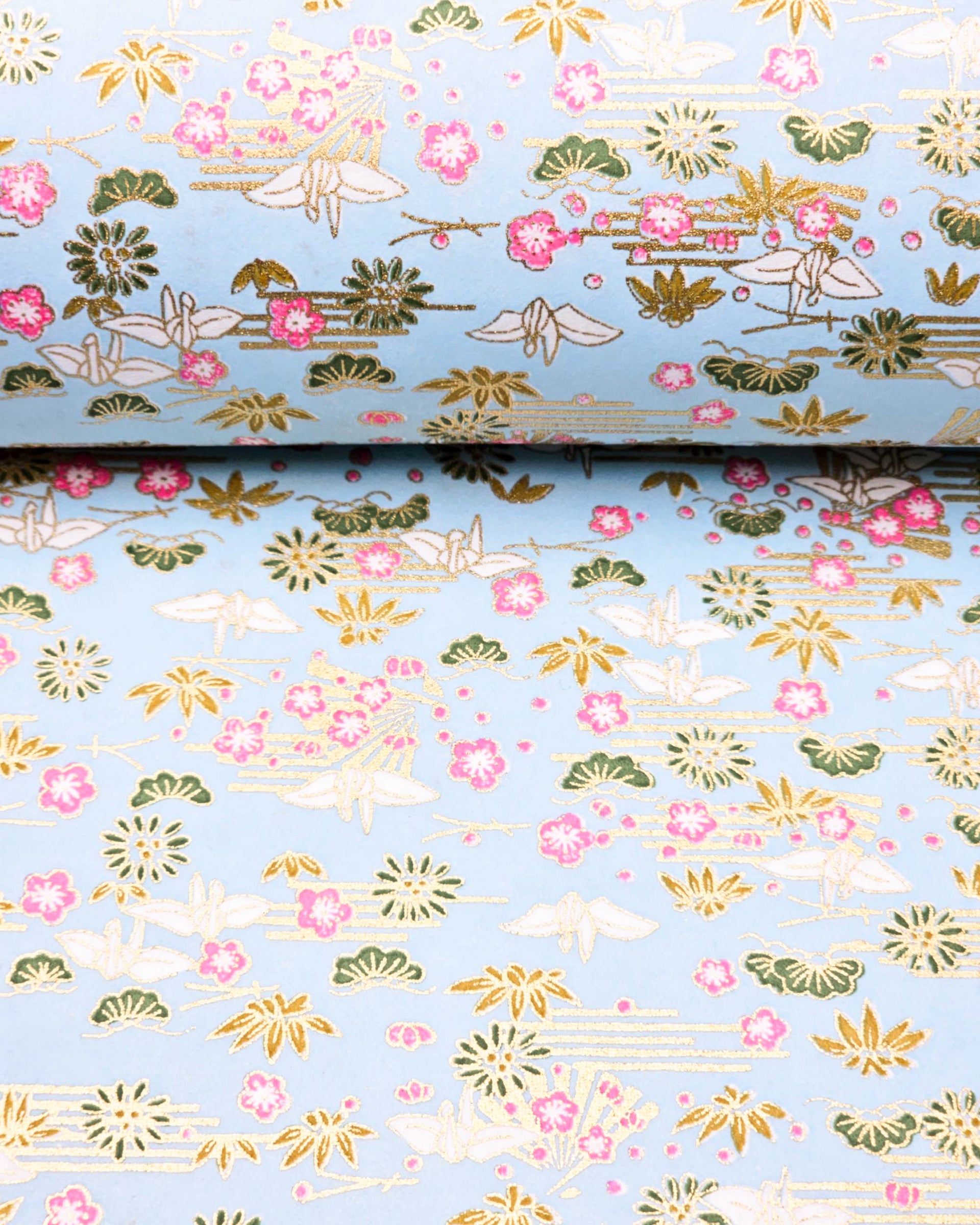 Japanese chiyogami paper featuring white origami cranes with green plants and pink plum blossoms on a light blue background with metallic gold details.