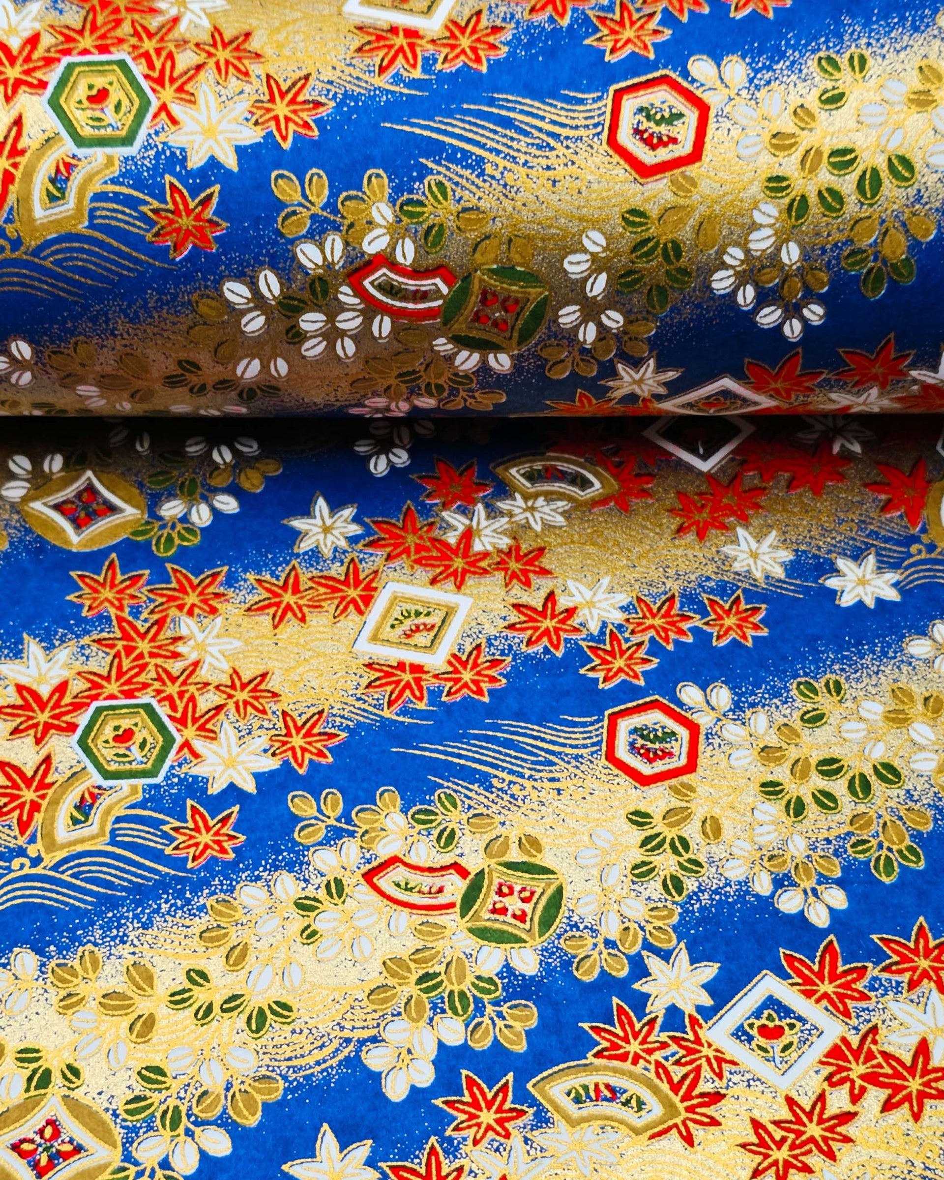 Japanese chiyogami paper featuring red and white maple leaves and traditional motifs on a blue and gold background with metallic gold details.