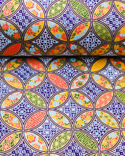Japanese chiyogami paper featuring an orange, yellow, and green shippo design filled with assorted floral and geometric designs on a dark blue background with metallic gold details. The centers of the shippos features assorted white floral outlines.
