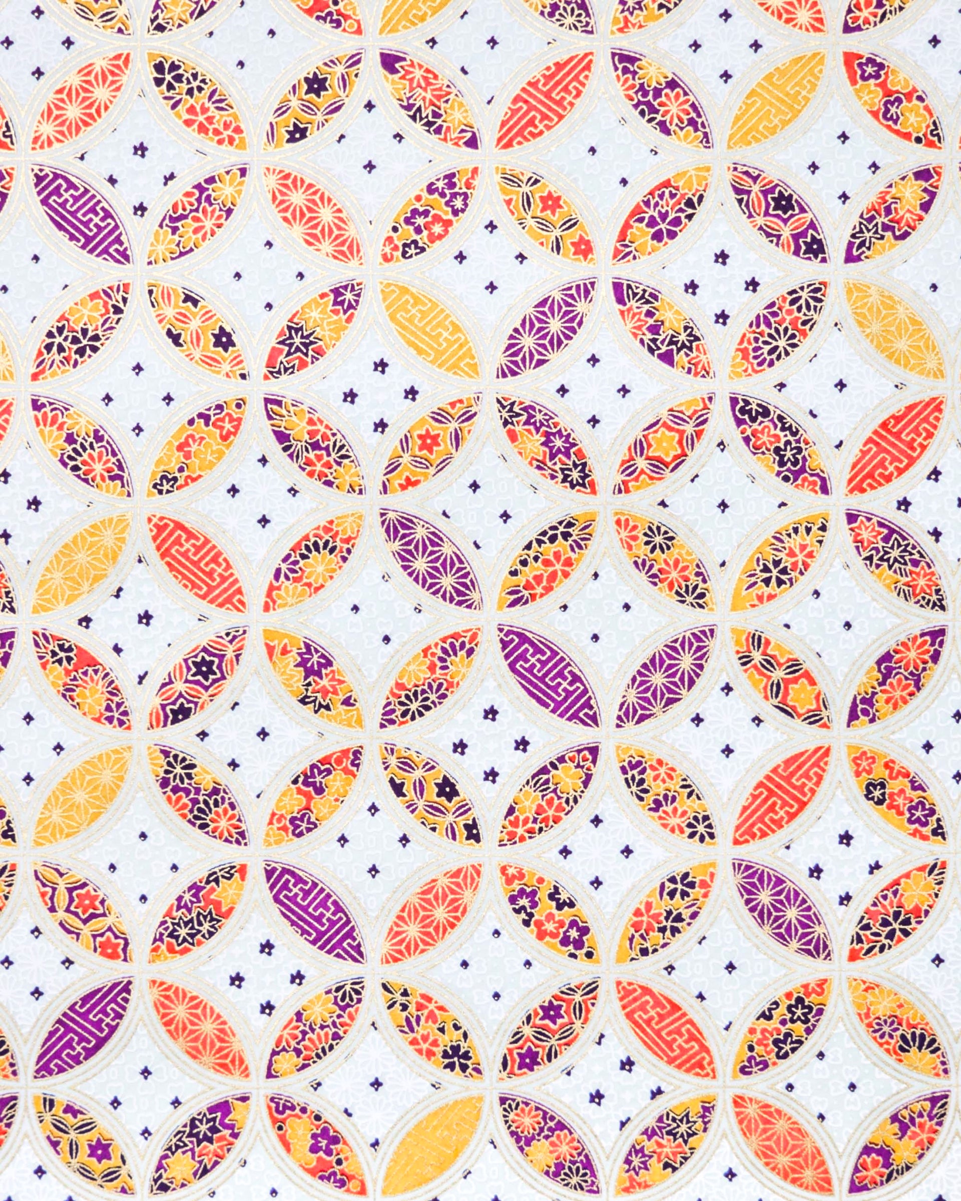 Japanese chiyogami paper featuring an orange, yellow, and purple shippo design filled with assorted floral and geometric designs on a light blue background with metallic gold details. The centers of the shippos features assorted white floral outlines.