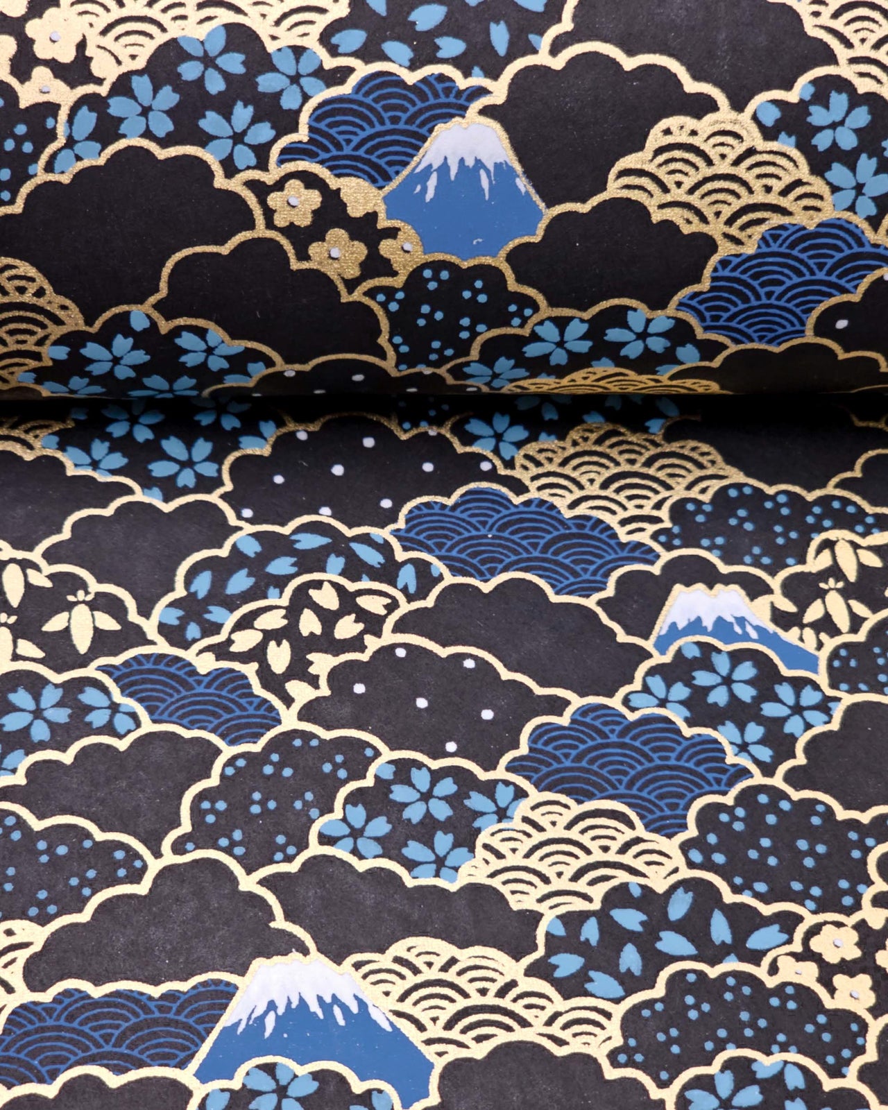 Japanese chiyogami paper featuring blue Mt Fuji and gold clouds filled with assorted gold and blue geometric and flower designs on a black background.