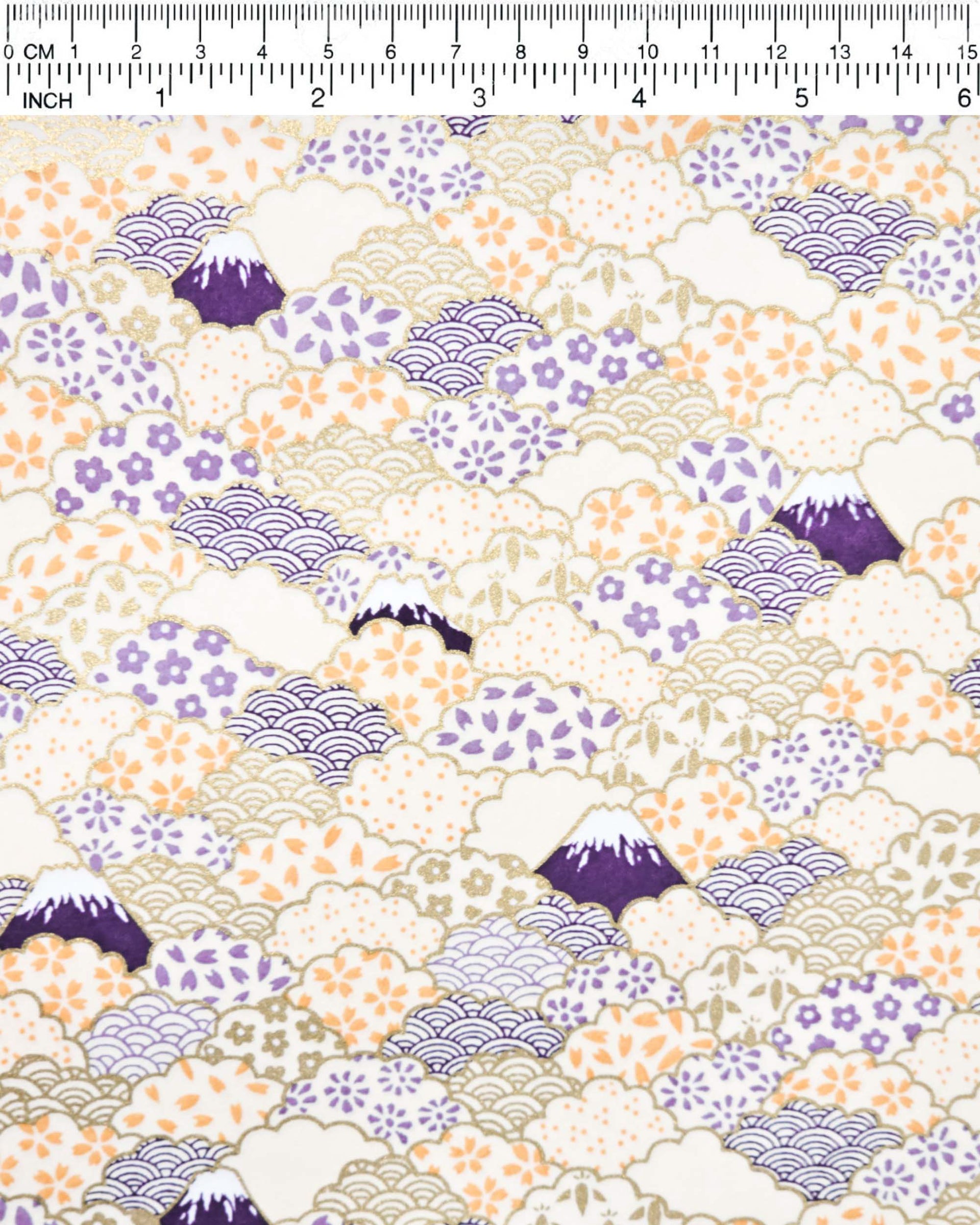 Japanese chiyogami paper featuring dark blue Mt Fuji and gold clouds filled with assorted gold, orange, and purple geometric and flower designs on a white background.