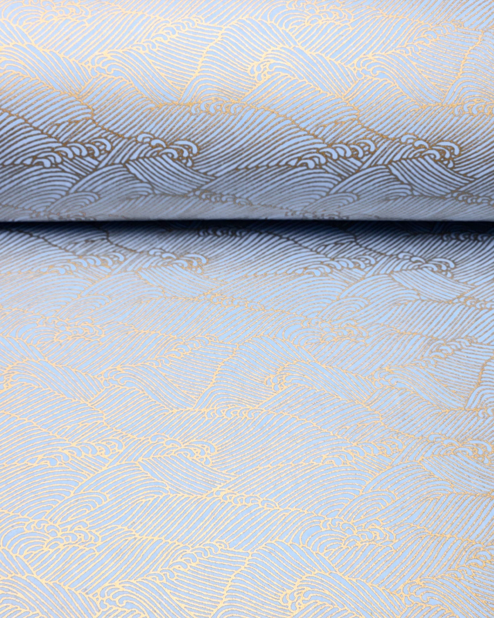 Japanese chiyogami paper featuring small metallic gold waves (aranami) on a light blue background. 