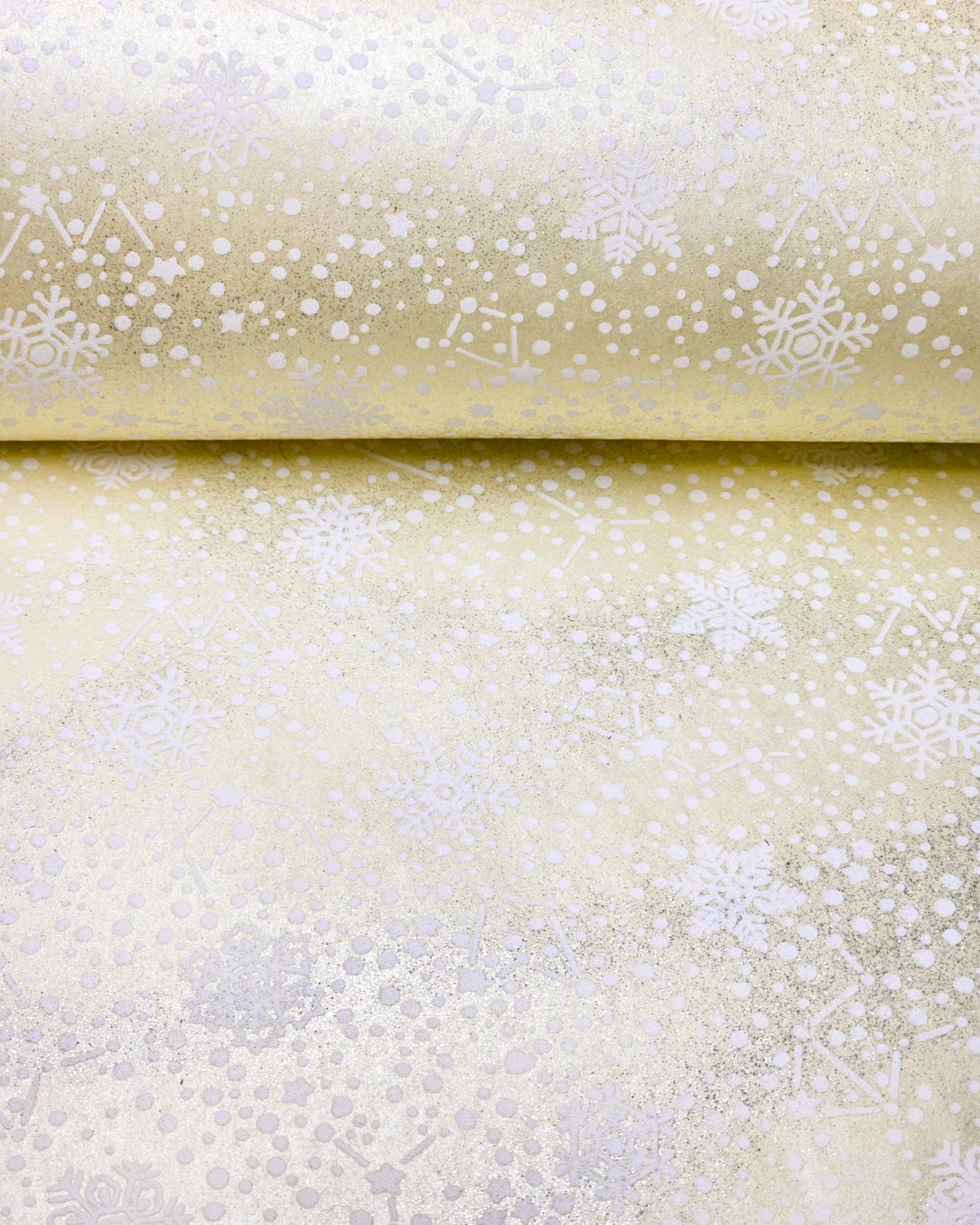 Japanese chiyogami paper featuring assorted white snowflakes and star constellations on a pearlescent light yellow background with metallic silver glitter details.