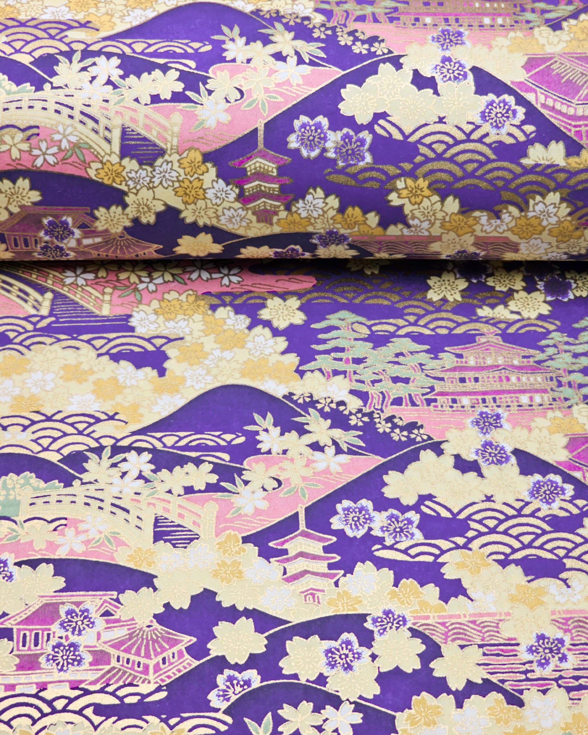 Japanese chiyogami paper featuring a traditional Japanese landscape with pagodas, temples, bridges, mountains, cherry blossoms, pine trees, and seigaiha (wave crests) patterns in yellow, pink, lavender, and mint green on a deep purple background with metallic gold details.