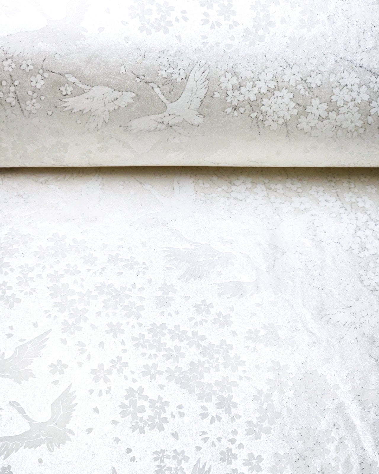 Japanese chiyogami paper featuring white flying cranes and plum and cherry blossoms on a pearlescent white background with metallic silver accents that create a fine glitter-like effect.