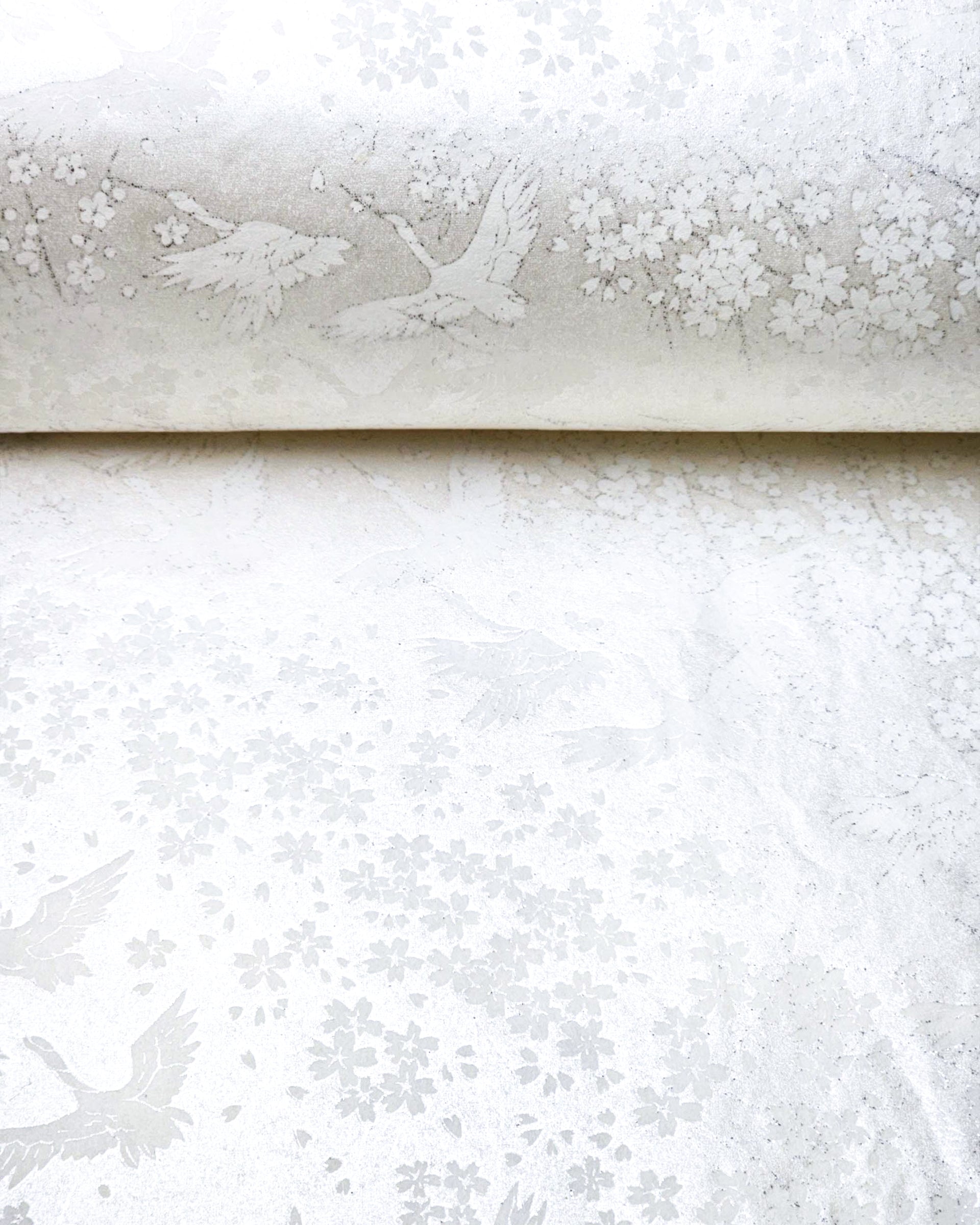 Japanese chiyogami paper featuring white flying cranes and plum and cherry blossoms on a pearlescent white background with metallic silver accents that create a fine glitter-like effect.