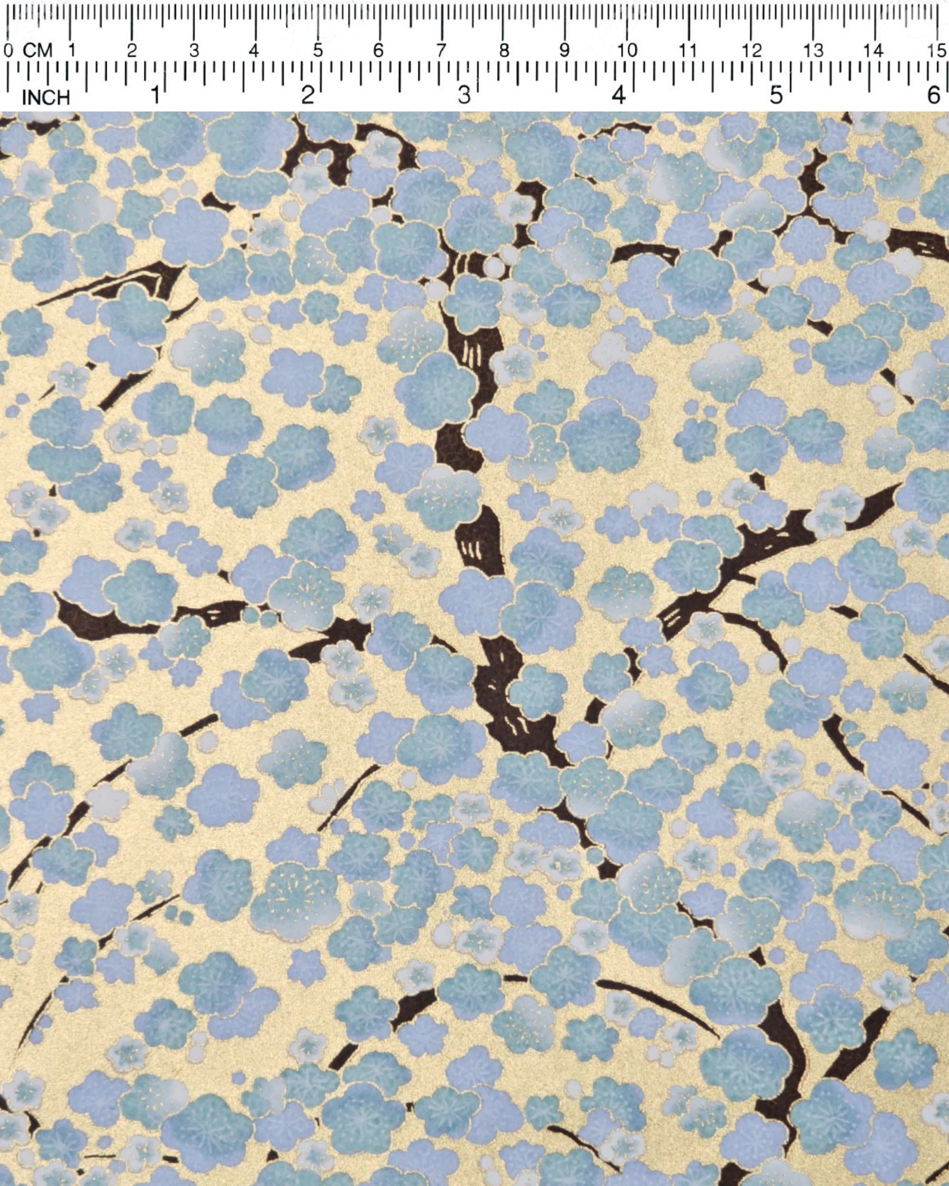 Japanese chiyogami paper featuring light blue and white plum blossom trees with dark brown branches on a gold background with metallic gold details.