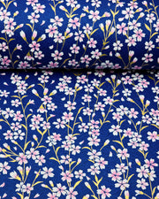 Japanese chiyogami paper featuring pink and white cherry blossoms with metallic gold stems and leaves on a dark blue background, shown rolled to highlight the design.
