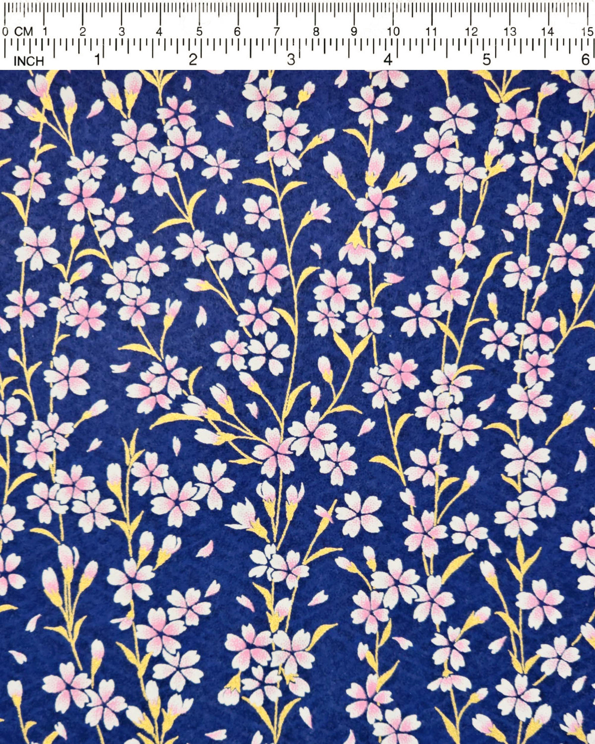 Japanese chiyogami paper featuring pink and white cherry blossoms with metallic gold stems and leaves on a dark blue background, shown next to a ruler for size reference.