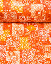 Japanese chiyogami paper featuring a patchwork-style arrangement of assorted floral and traditional Japanese patterns in various shades of orange and white, shown rolled to highlight the design.