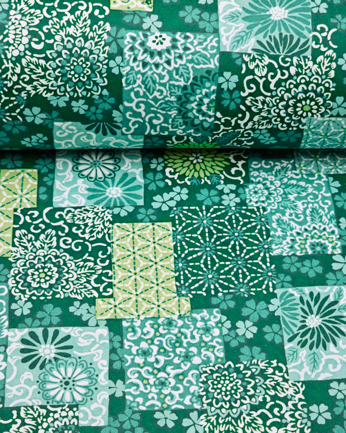 Japanese chiyogami paper featuring a patchwork-style arrangement of assorted floral and traditional Japanese patterns in various shades of green and white, shown rolled to highlight the design.