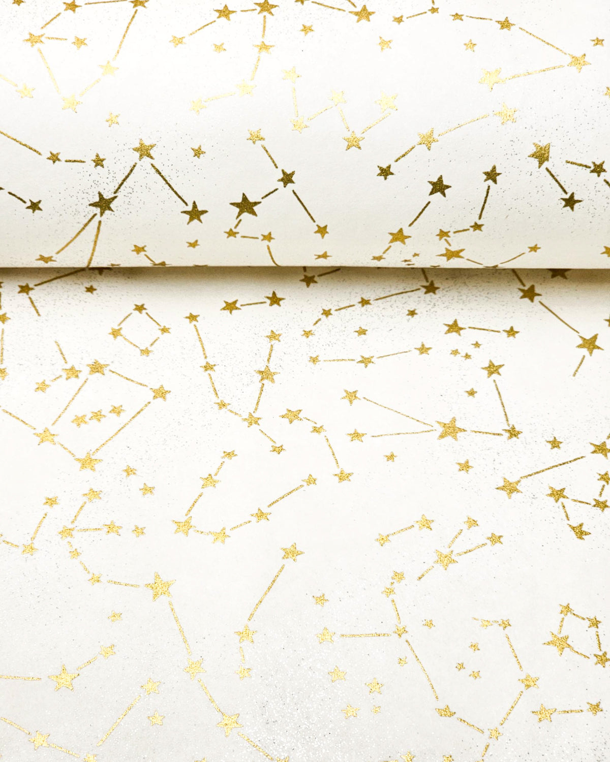 Japanese chiyogami paper featuring metallic gold stars and constellations scattered across a white background with shimmering metallic silver stardust, shown rolled to highlight the design.