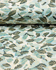 Japanese chiyogami paper featuring dark green, light blue-green, and white leaves on a white background with metallic gold details, shown rolled to highlight the design.