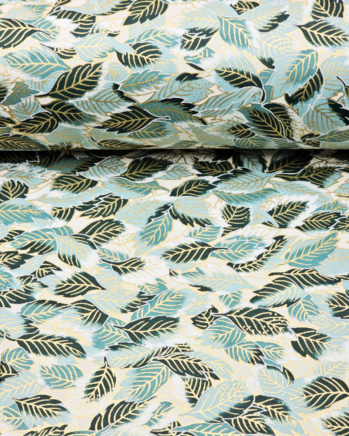 Japanese chiyogami paper featuring dark green, light blue-green, and white leaves on a white background with metallic gold details, shown rolled to highlight the design.