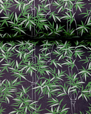 Japanese chiyogami paper featuring bamboo stalks outlined in gray with dark and light green bamboo leaves on a black background, shown rolled to highlight the design.