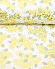 Japanese chiyogami paper featuring yellow and white roses with light green leaves and smaller white flowers on a white background with metallic gold details, shown rolled to highlight the design.