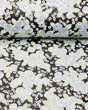 Japanese chiyogami paper featuring blue and white roses with light green leaves and smaller white flowers on a black background with metallic gold details, shown rolled to highlight the design.