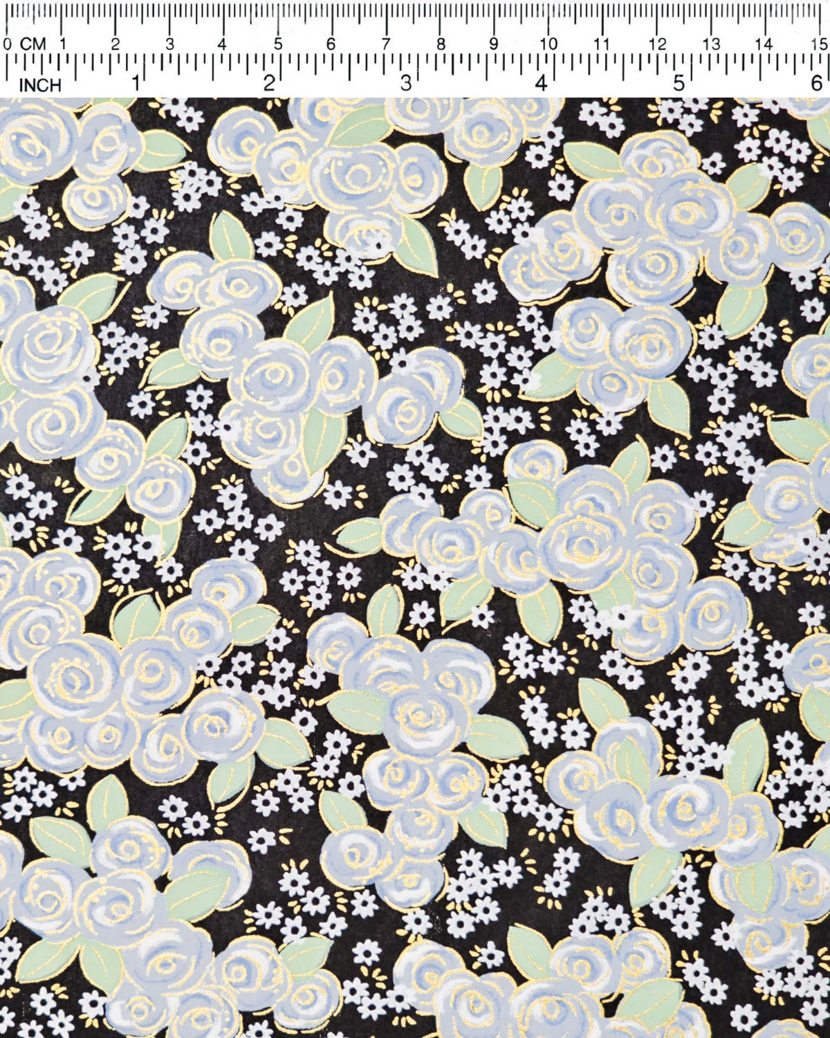 Japanese chiyogami paper featuring blue and white roses with light green leaves and smaller white flowers on a black background with metallic gold details, shown next to a ruler for size reference.