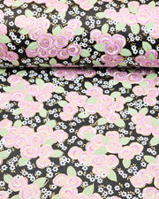 Japanese chiyogami paper featuring purple and white roses with light green leaves and smaller white flowers on a black background with metallic gold details, shown rolled to highlight the design.