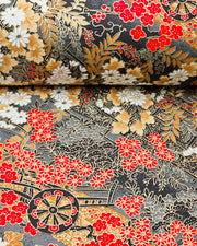 Japanese chiyogami paper featuring black flower carts with assorted red, white, and gray flowers with brown leaves on a gray background with metallic gold details, shown rolled to highlight the design.
