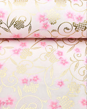 Japanese chiyogami paper featuring pink cherry blossoms alongside gold cherry blossoms and leaves decorated with a traditional kanoko (fawn) pattern on a light pink background, shown rolled to highlight the design.
