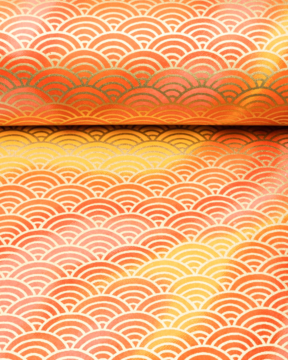 Japanese chiyogami paper featuring a large metallic gold traditional seigaiha (wave crest) pattern on a flowing background in various shades of orange, shown rolled to highlight the design.