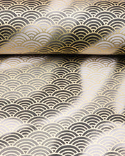 Japanese chiyogami paper featuring a large metallic gold traditional seigaiha (wave crest) pattern on a flowing background in various shades of gray and black, shown rolled to highlight the design.