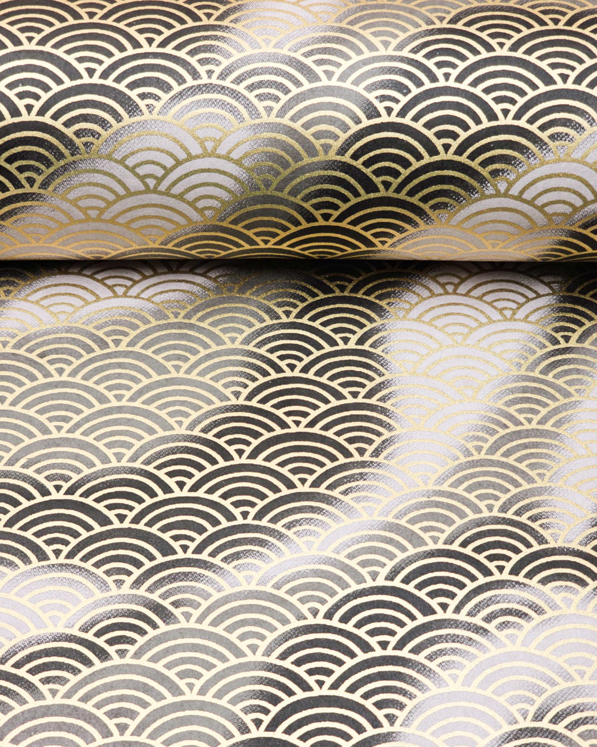 Japanese chiyogami paper featuring a large metallic gold traditional seigaiha (wave crest) pattern on a flowing background in various shades of gray and black, shown rolled to highlight the design.