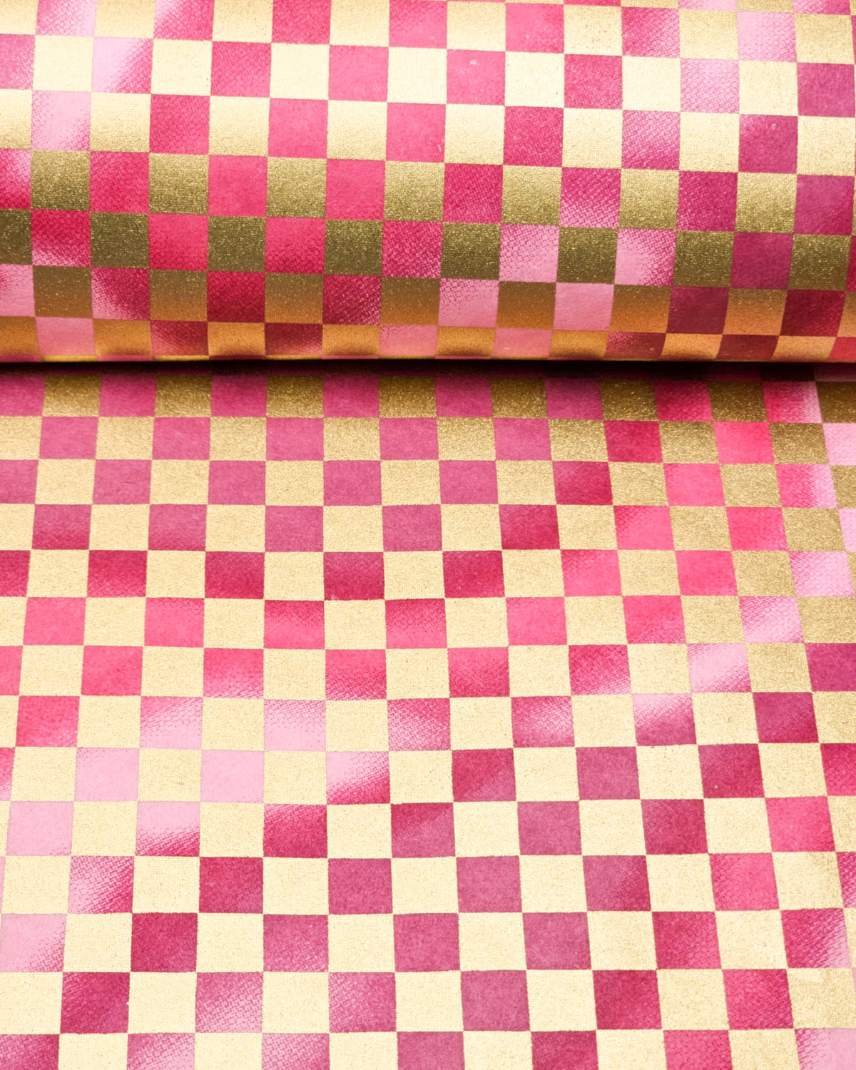 Japanese chiyogami paper featuring a large metallic gold traditional ichimatsu (checker) pattern on a flowing background in various shades of magenta pink, shown rolled to highlight the design.