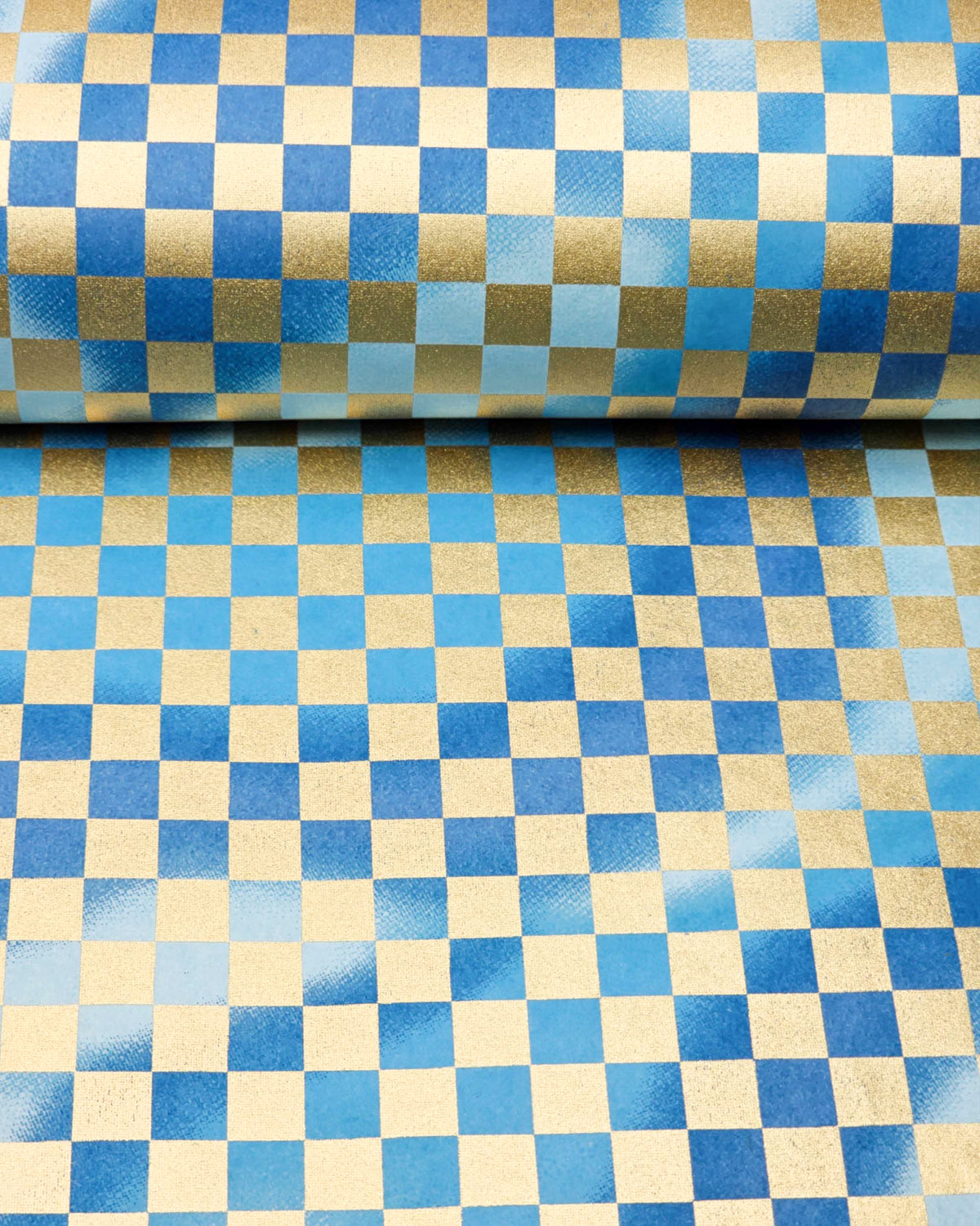 Japanese chiyogami paper featuring a large metallic gold traditional ichimatsu (checker) pattern on a flowing background in various shades of blue, shown rolled to highlight the design.