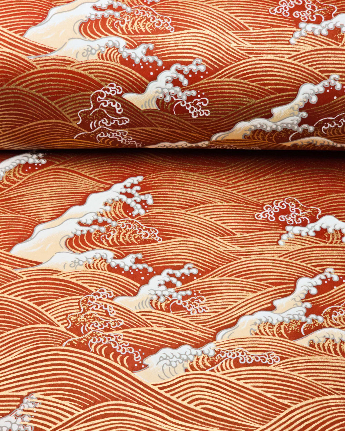 Japanese chiyogami paper featuring metallic gold waves with beige and white detailed waves on a red background, shown rolled to highlight the design.