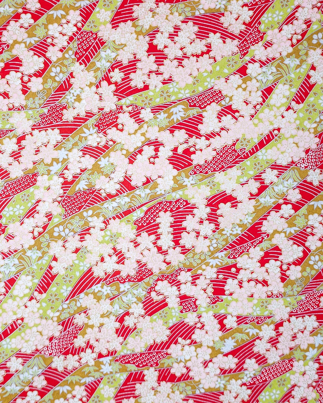 Japanese chiyogami paper featuring pink plum and cherry blossoms with flowing green ribbons on a red and silver seigaihai background with metallic gold details.