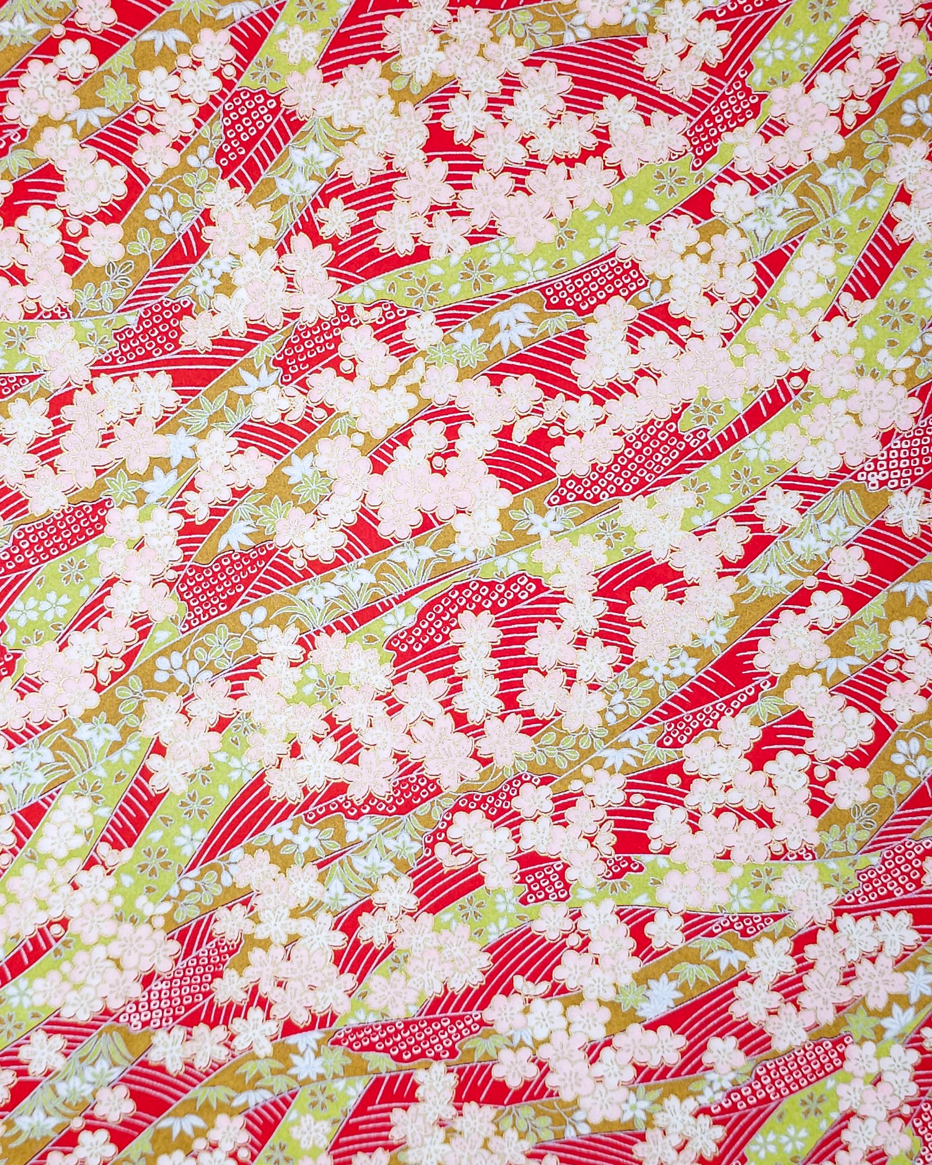 Japanese chiyogami paper featuring pink plum and cherry blossoms with flowing green ribbons on a red and silver seigaihai background with metallic gold details.