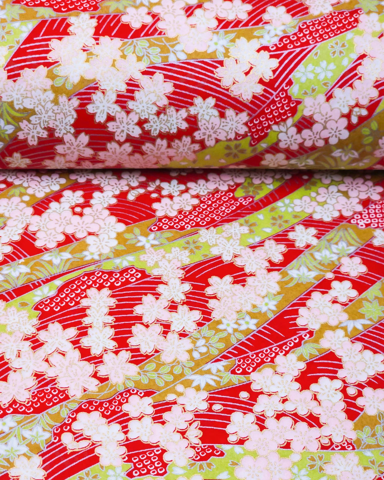 Japanese chiyogami paper featuring pink plum and cherry blossoms with flowing green ribbons on a red and silver seigaihai background with metallic gold details.