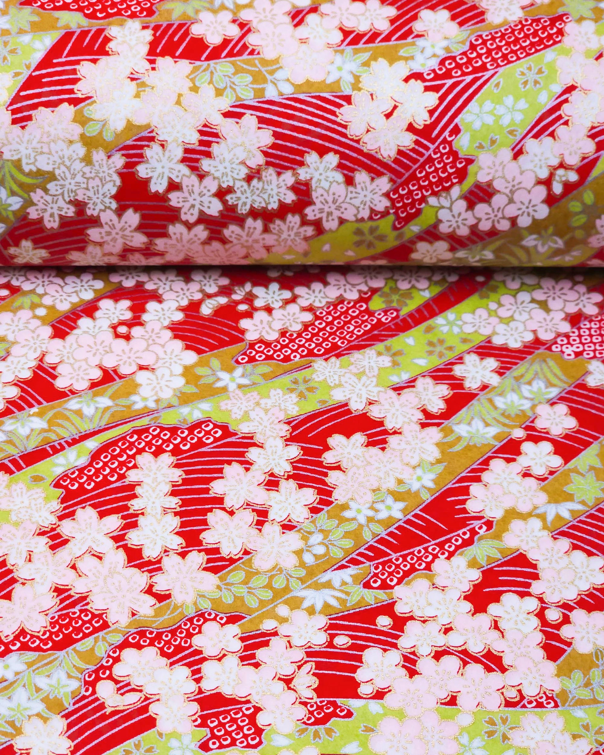 Japanese chiyogami paper featuring pink plum and cherry blossoms with flowing green ribbons on a red and silver seigaihai background with metallic gold details.