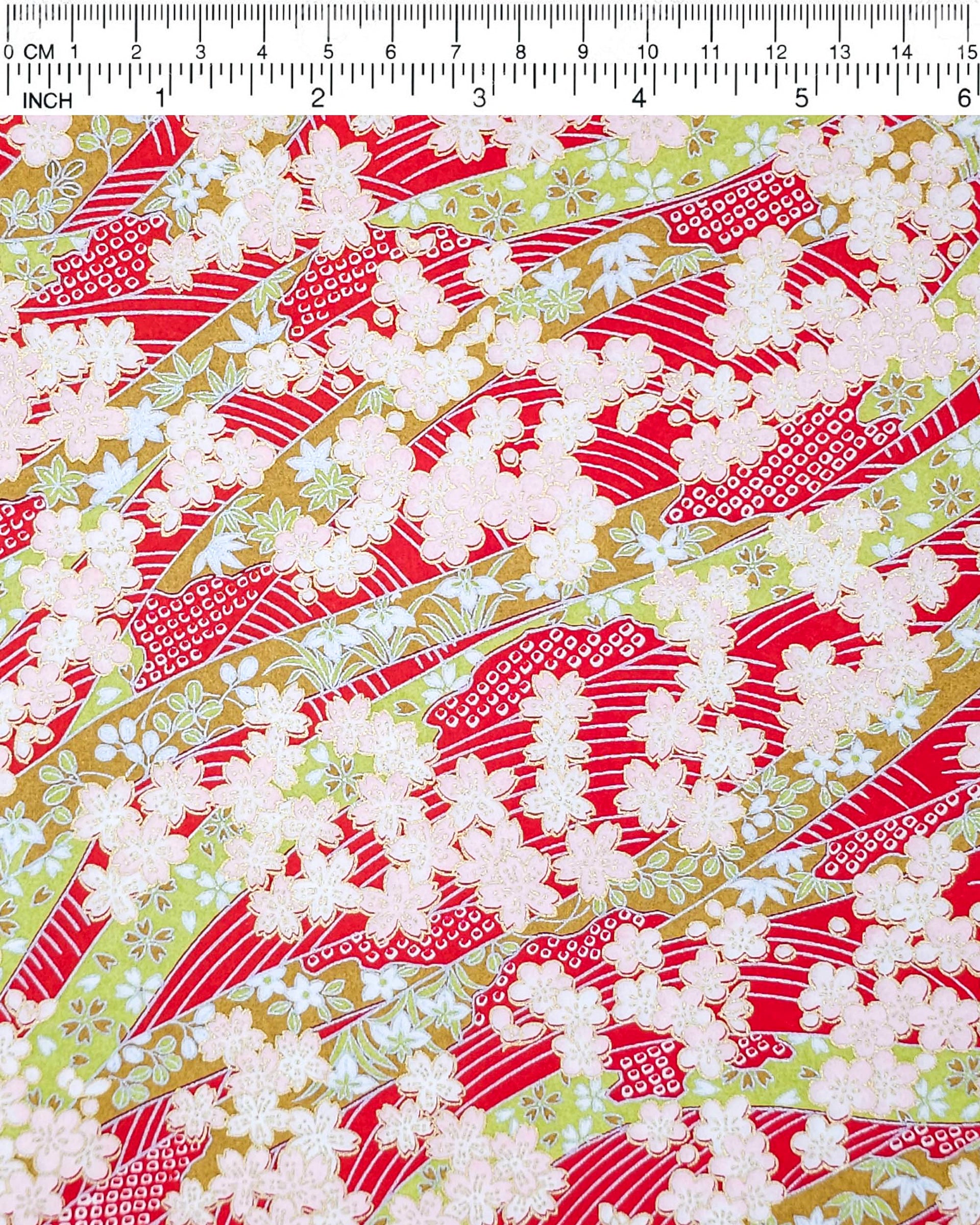Japanese chiyogami paper featuring pink plum and cherry blossoms with flowing green ribbons on a red and silver seigaihai background with metallic gold details.