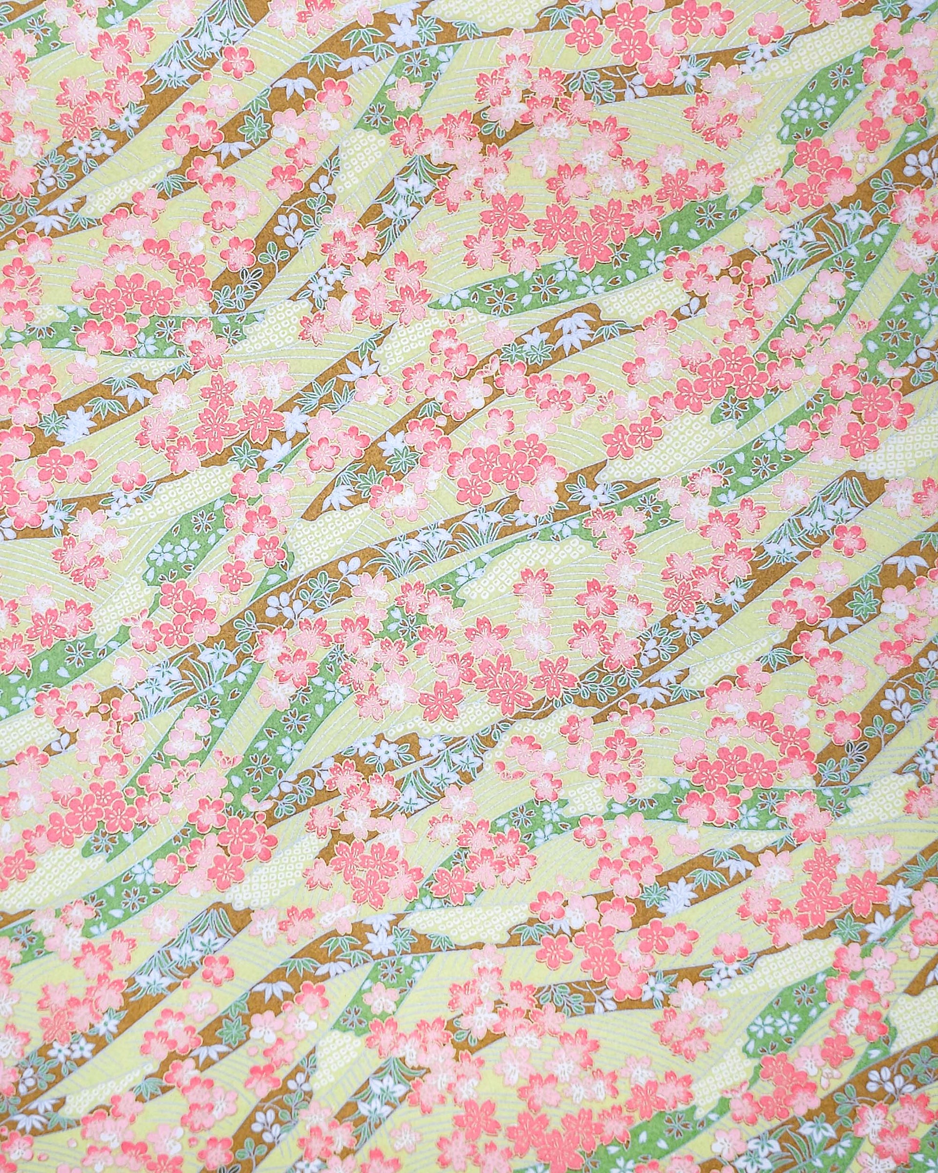 Japanese chiyogami paper featuring pink plum and cherry blossoms with flowing green and brown ribbons on a light green background with metallic gold details.