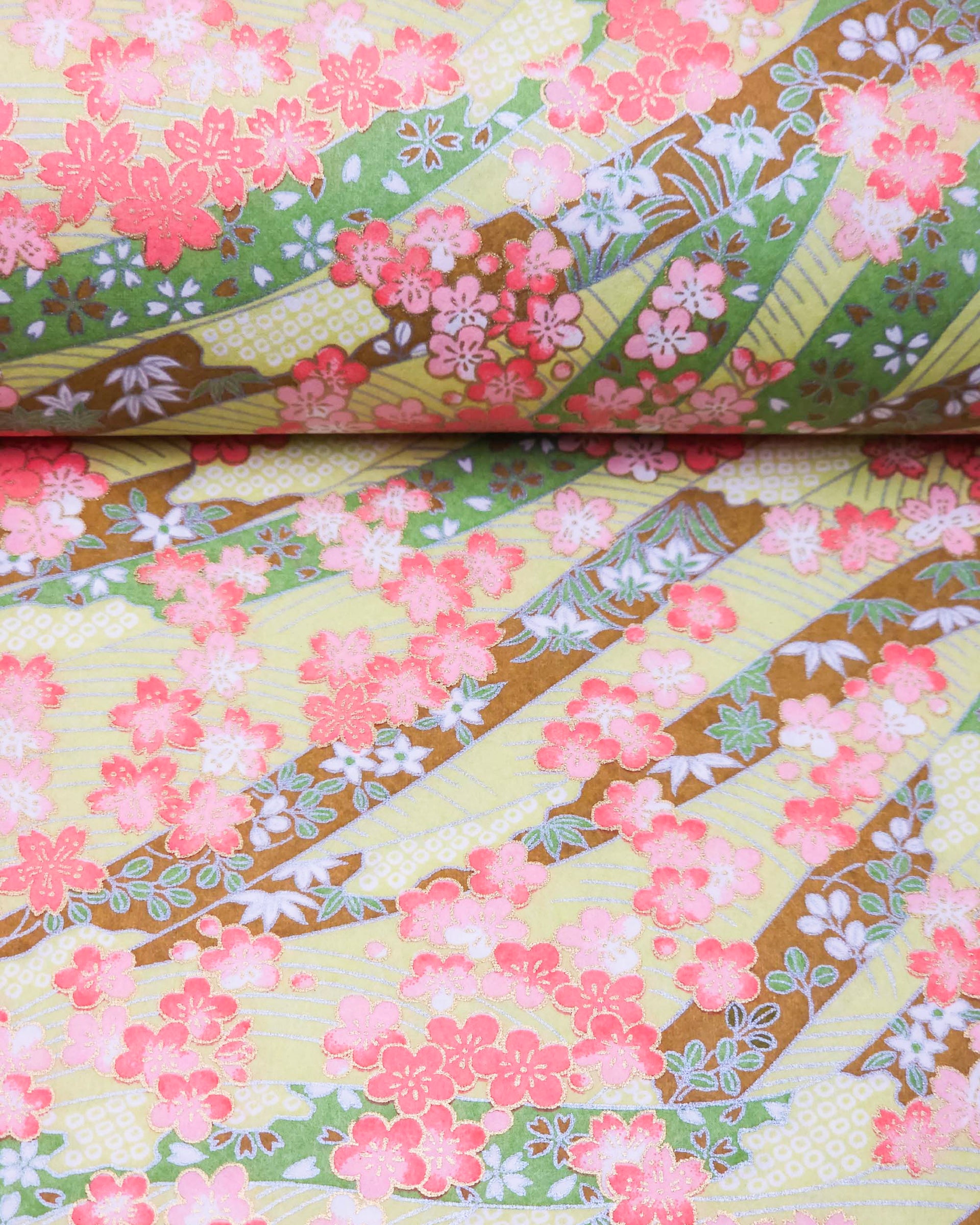 Japanese chiyogami paper featuring pink plum and cherry blossoms with flowing green and brown ribbons on a light green background with metallic gold details.