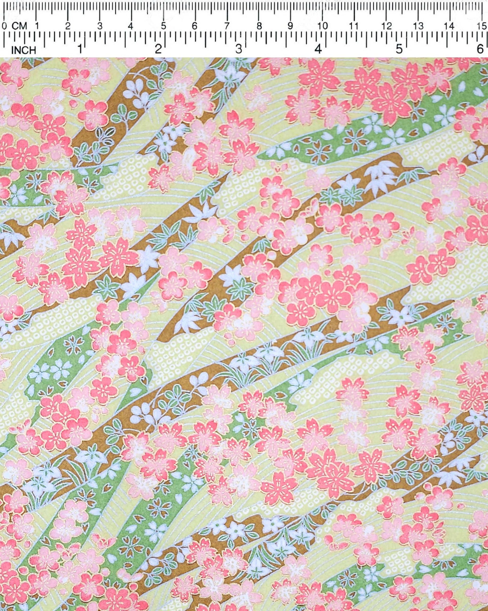 Japanese chiyogami paper featuring pink plum and cherry blossoms with flowing green and brown ribbons on a light green background with metallic gold details.