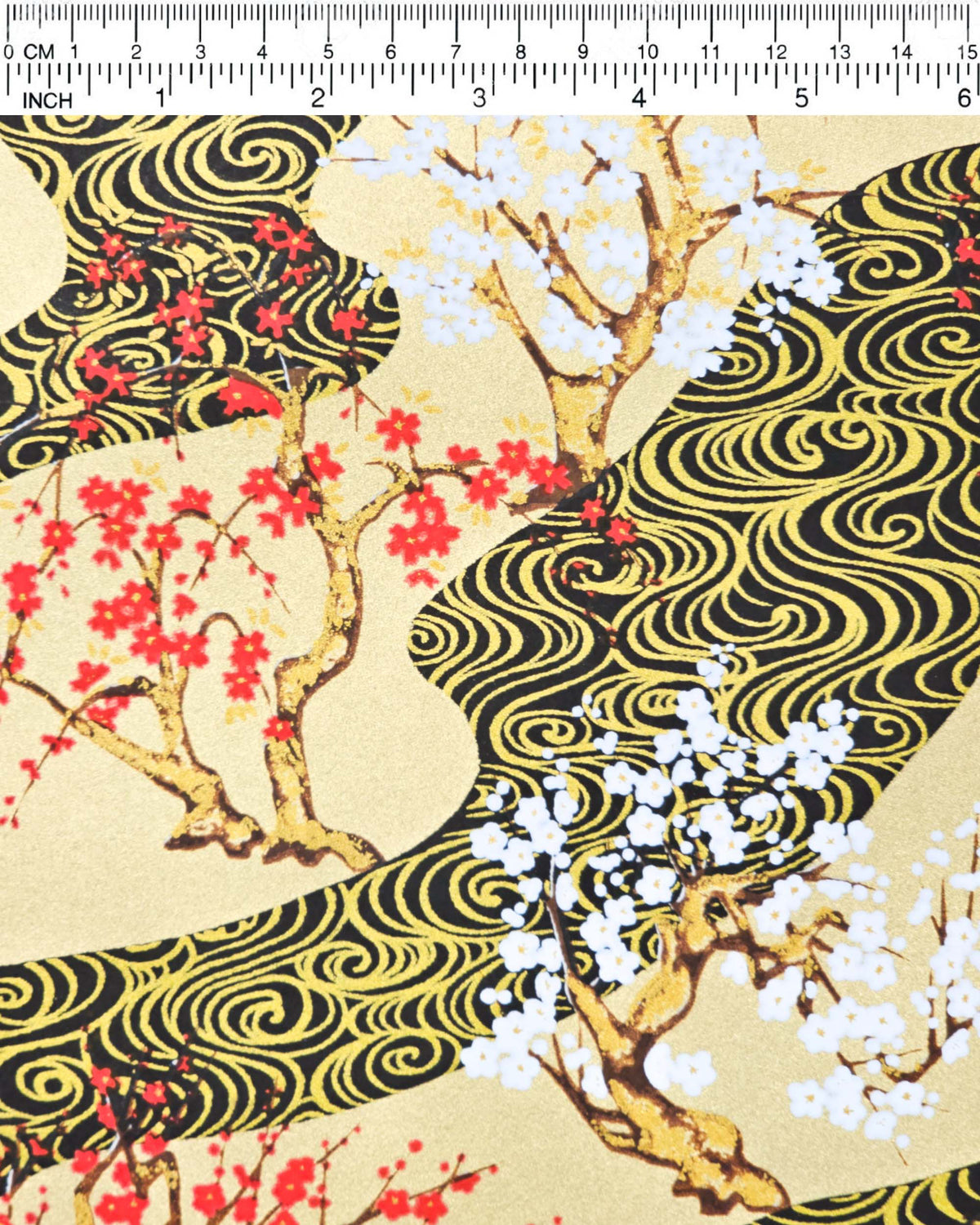 Japanese chiyogami paper featuring red and white plum and cherry blossom trees set against a metallic gold and black water ripple pattern on a gold background, shown next to a ruler for size reference.