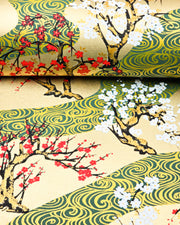 Japanese chiyogami paper featuring red and white plum and cherry blossom trees set against a metallic gold and green water ripple pattern on a gold background, shown rolled to highlight the design.