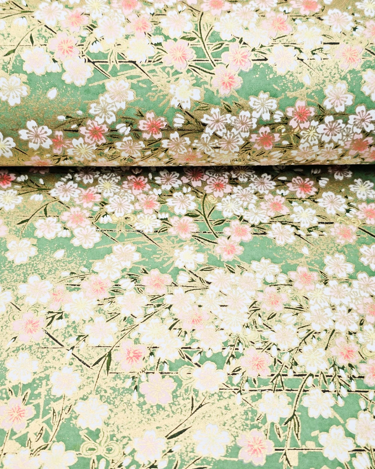 Japanese chiyogami paper featuring light pink and white cherry blossoms on a green background with metallic gold details.
