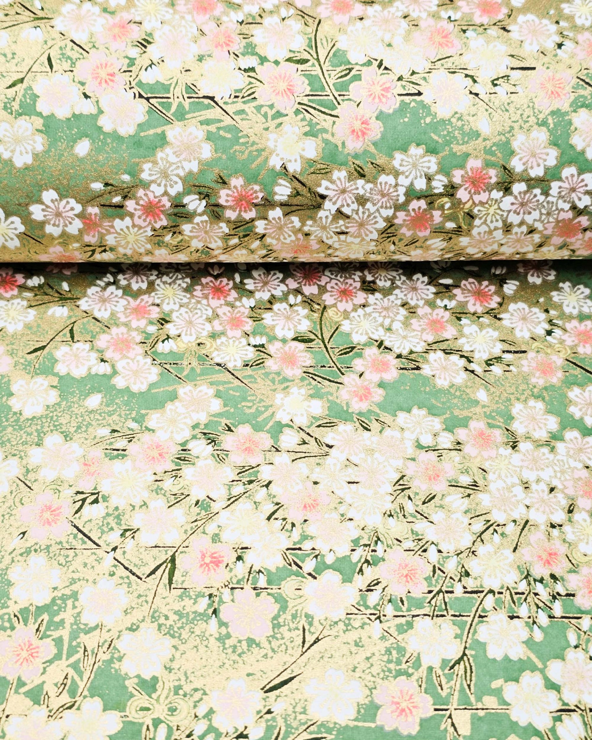 Japanese chiyogami paper featuring light pink and white cherry blossoms on a green background with metallic gold details.